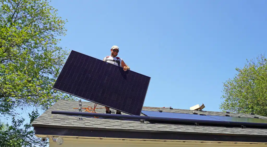 Sunnymac employee carries solar panel while walking on roof