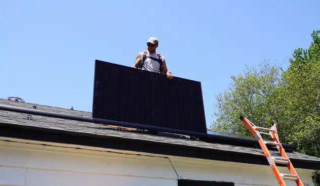 sunnymac solar installer on a roof holding a solar panel and wearing a safety harness